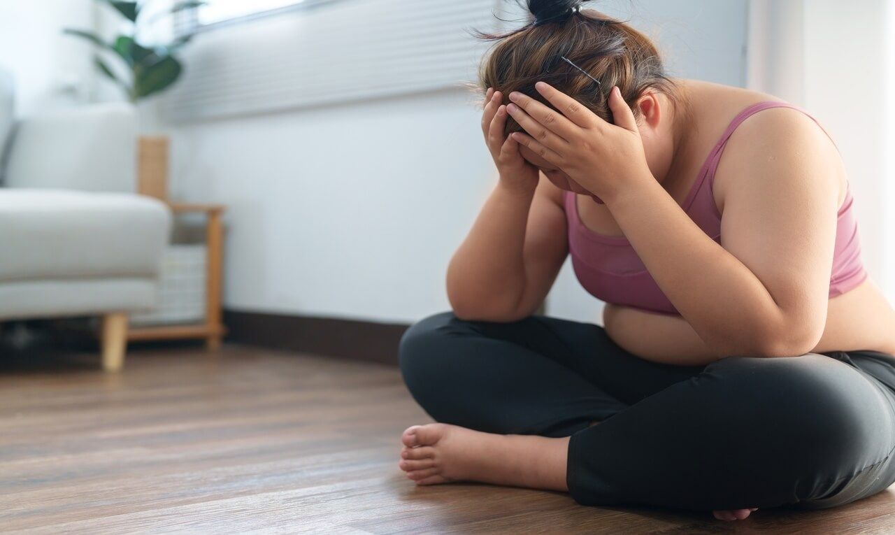 Person sitting on the floor, holding their head in distress in a bright living room.