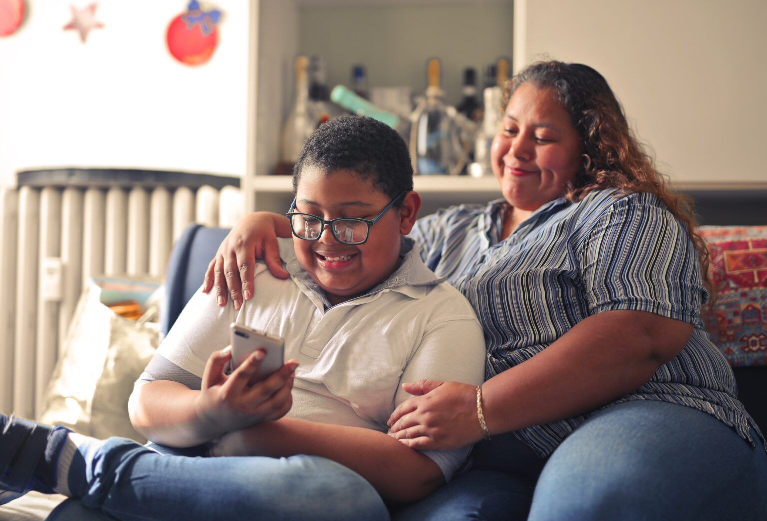 Duas pessoas sentadas em um sofá, sorrindo enquanto olham para um smartphone em uma sala de estar 