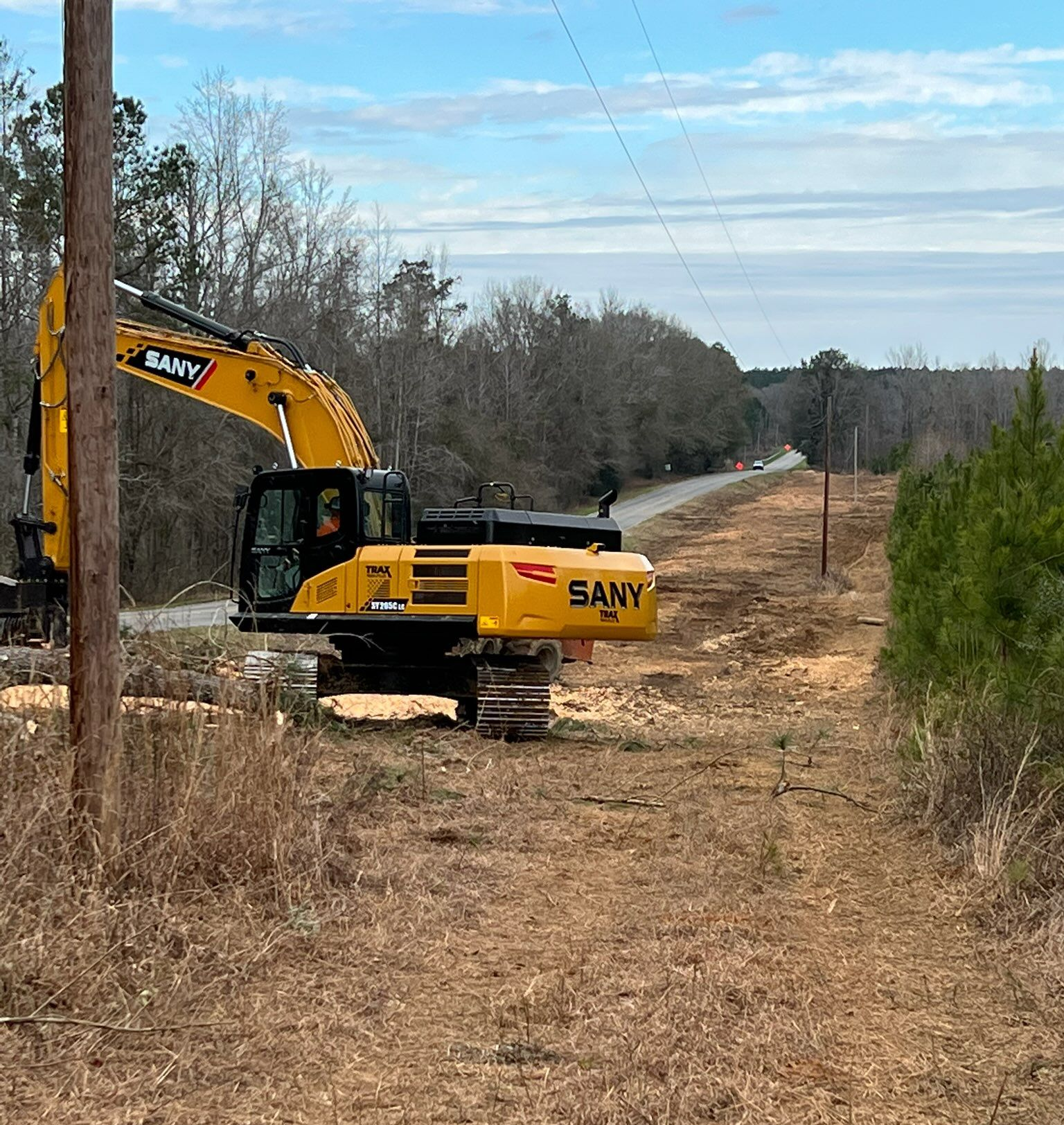 Excavator mulching brush in a wooded area, spraying debris and wood chips.