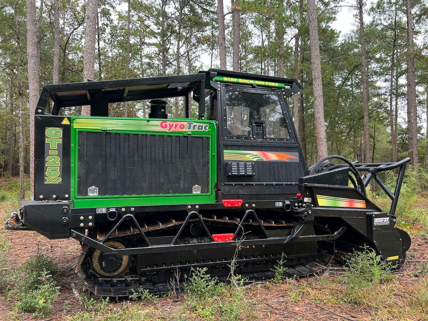 Green and black forestry harvester in a pine forest, with an excavator-style cutting arm.