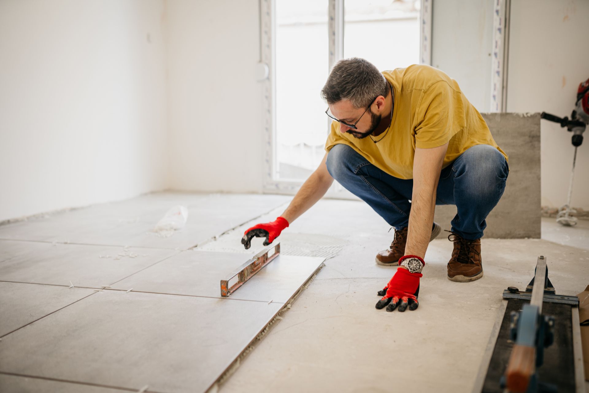 A man is measuring a tile floor with a level. A man is measuring a tile floor with a level.
