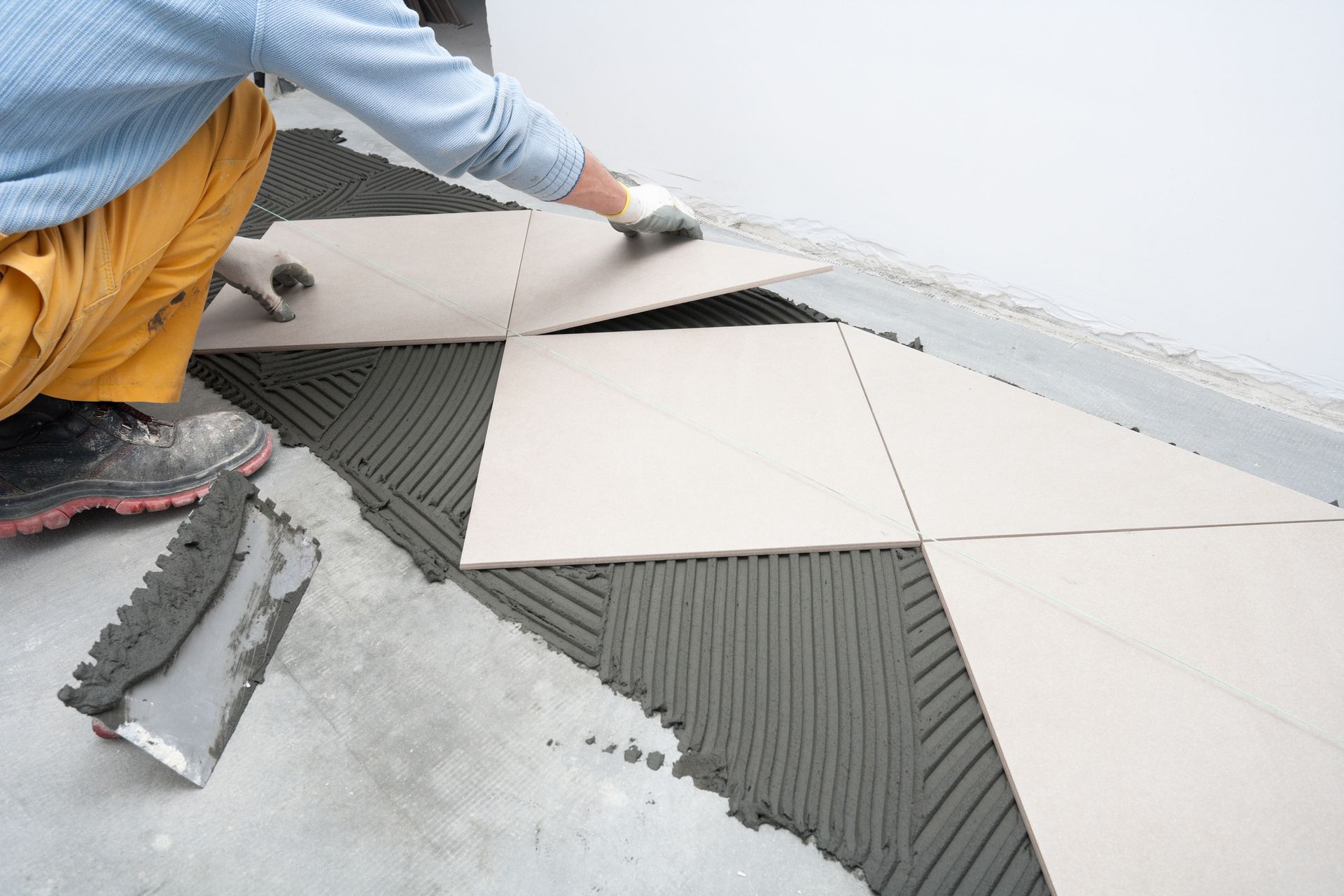 A man is laying tiles on a concrete floor A man is laying tiles on a concrete floor