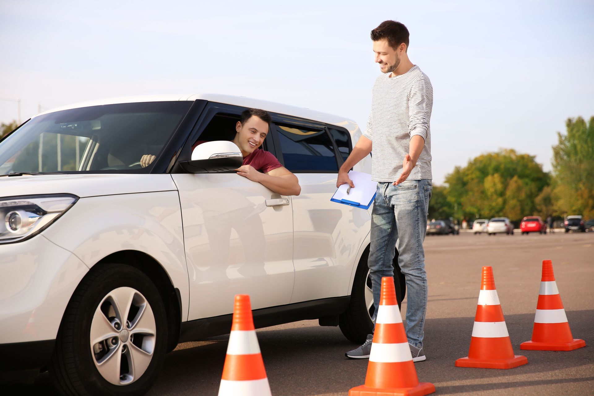 A man is teaching another man how to drive a car in a parking lot.
