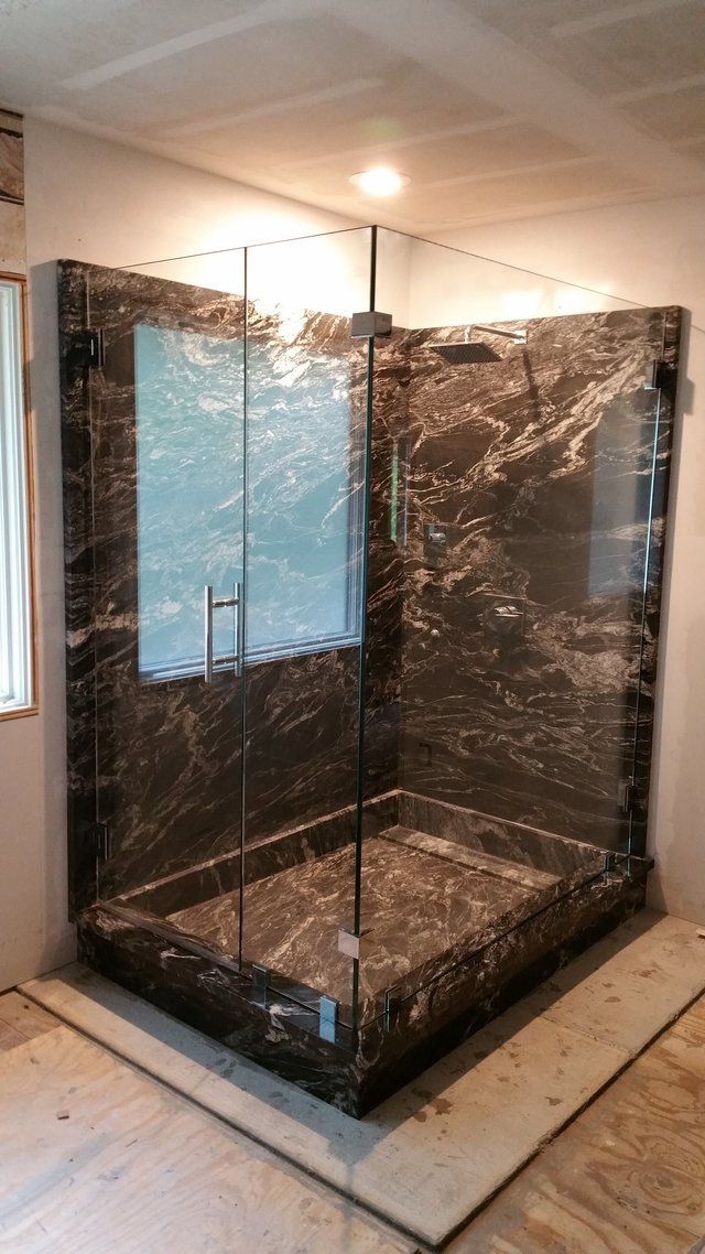 A custom shower with a marble-like finish. Glass doors and walls enclose the corner shower.