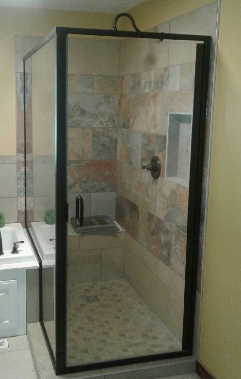 A black-framed glass shower with patterned tile walls. A small built-in shelf is visible inside.