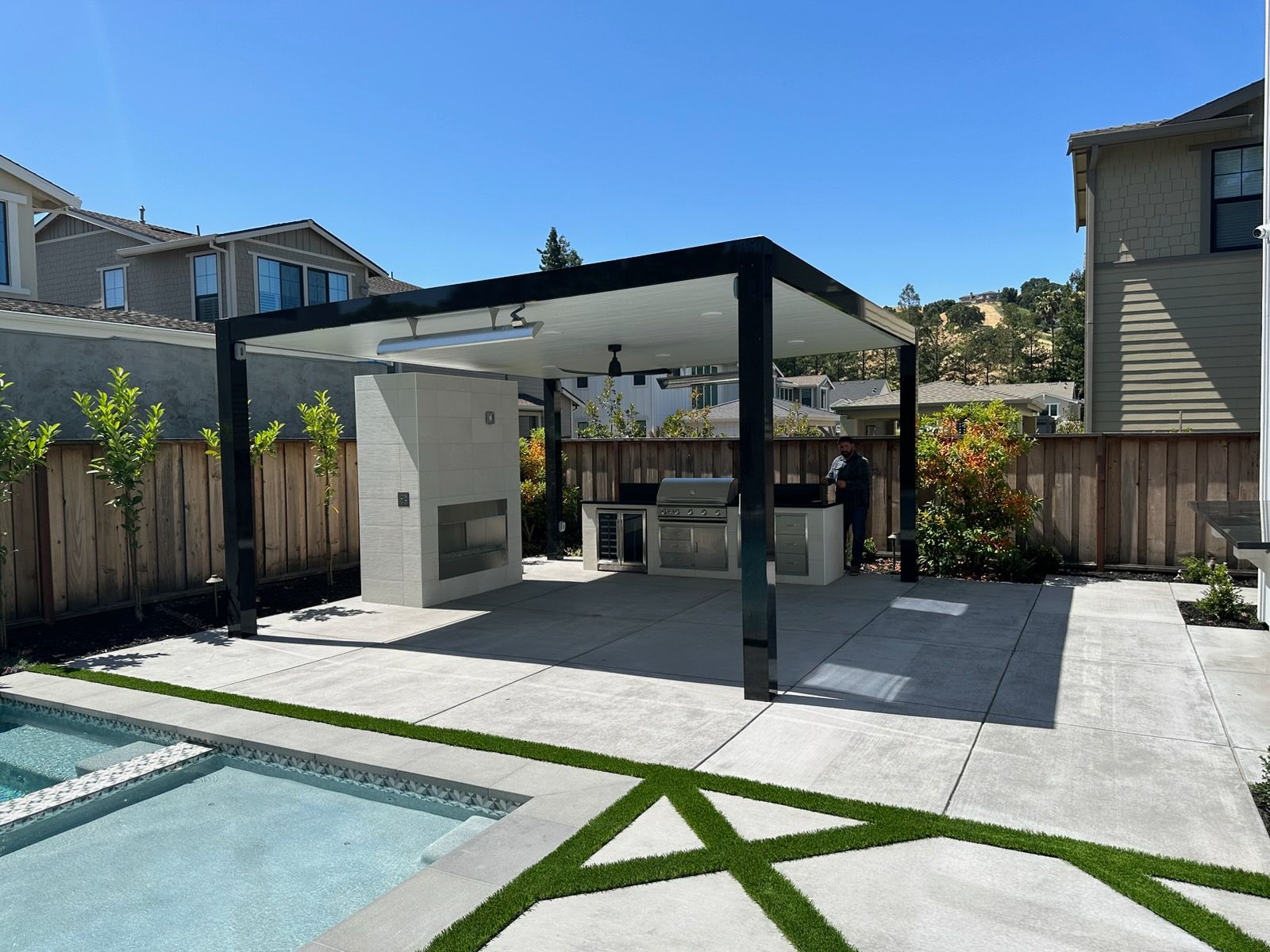 Outdoor patio with built-in grill, fireplace, and covered seating area next to a pool.