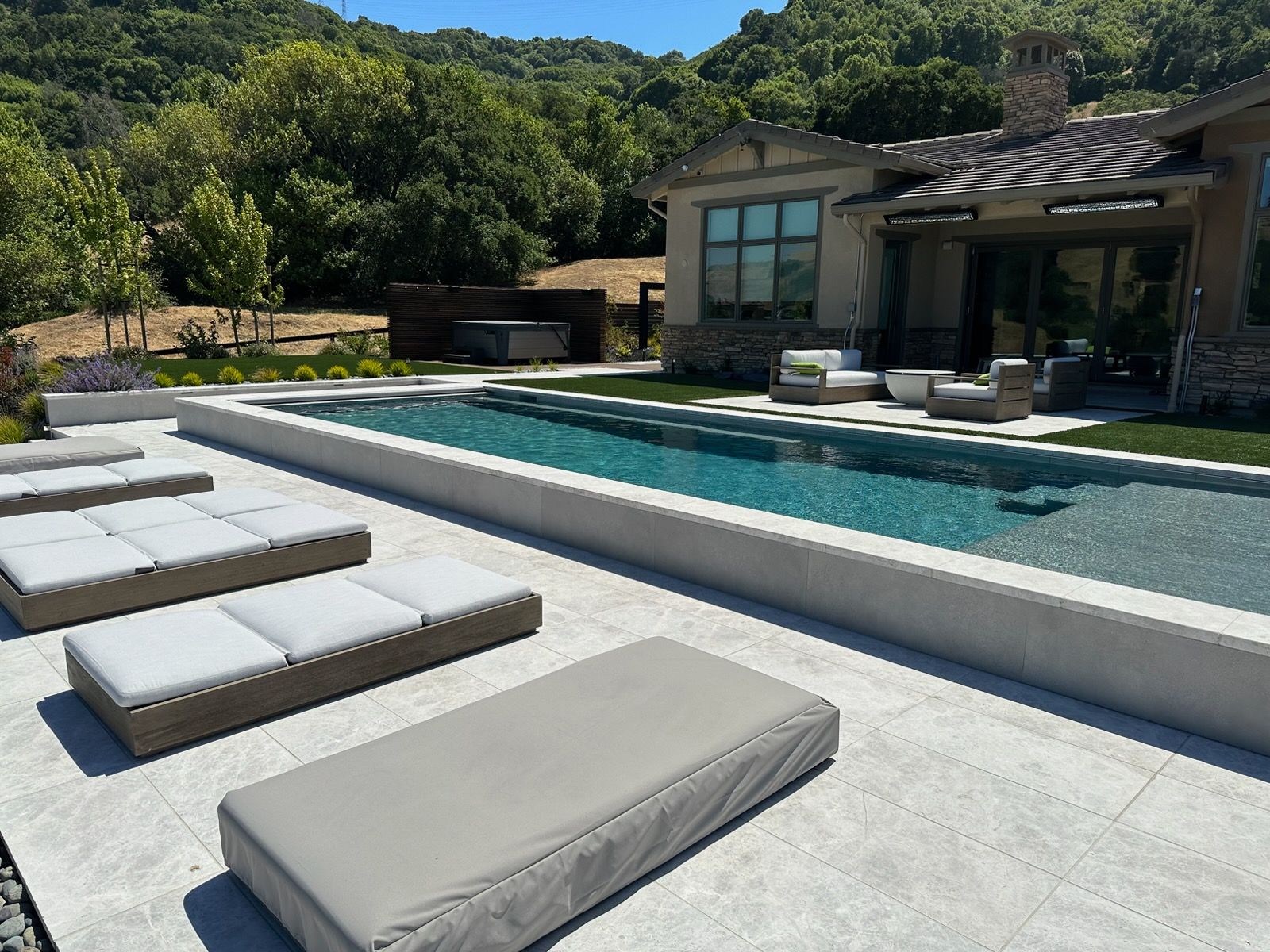 Modern home with a long pool, lounge chairs, and mountain backdrop on a sunny day.