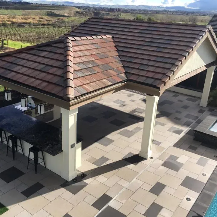 Patio with brown tile roof, outdoor kitchen, and stone patio by a pool, vineyard in background.