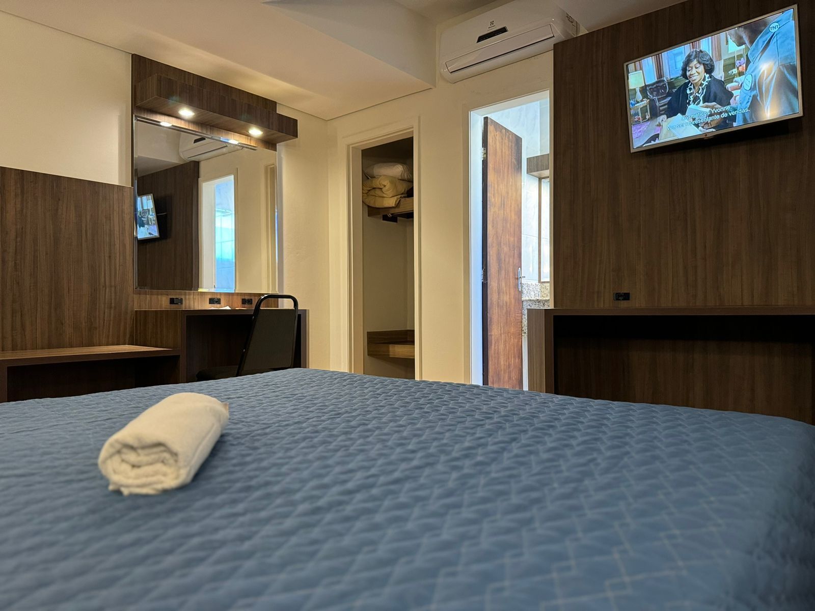 Um quarto de hotel com uma cama, televisão e uma toalha na cama.
