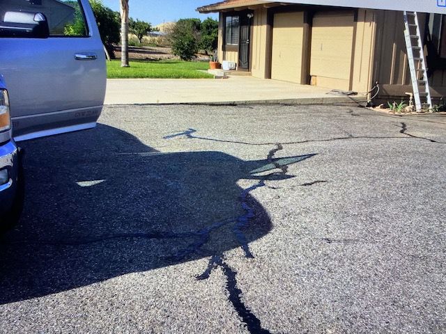 Silver truck casting a shadow on cracked asphalt. Building and lawn in background. Sunny day.