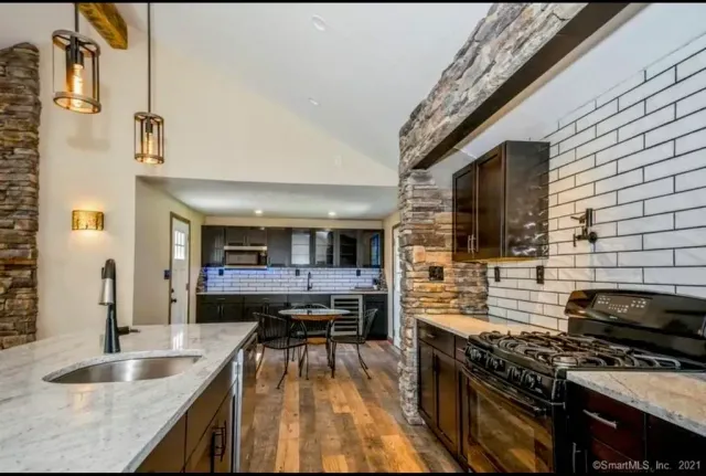 A kitchen with a stove , sink , and wooden floors