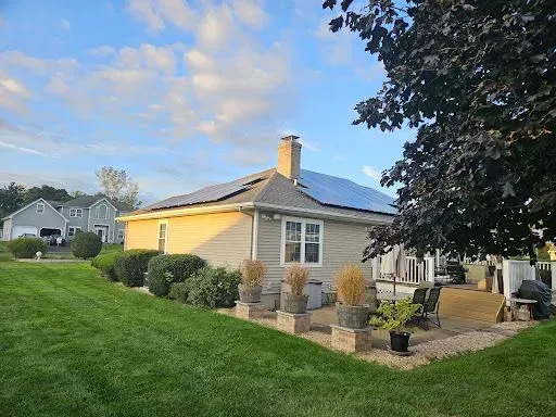 A house with solar panels on the roof is sitting on top of a lush green lawn.