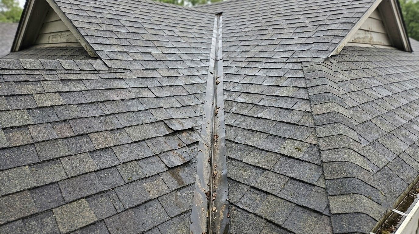 Residential roof with gray shingles and a central ridge vent, viewed from above.