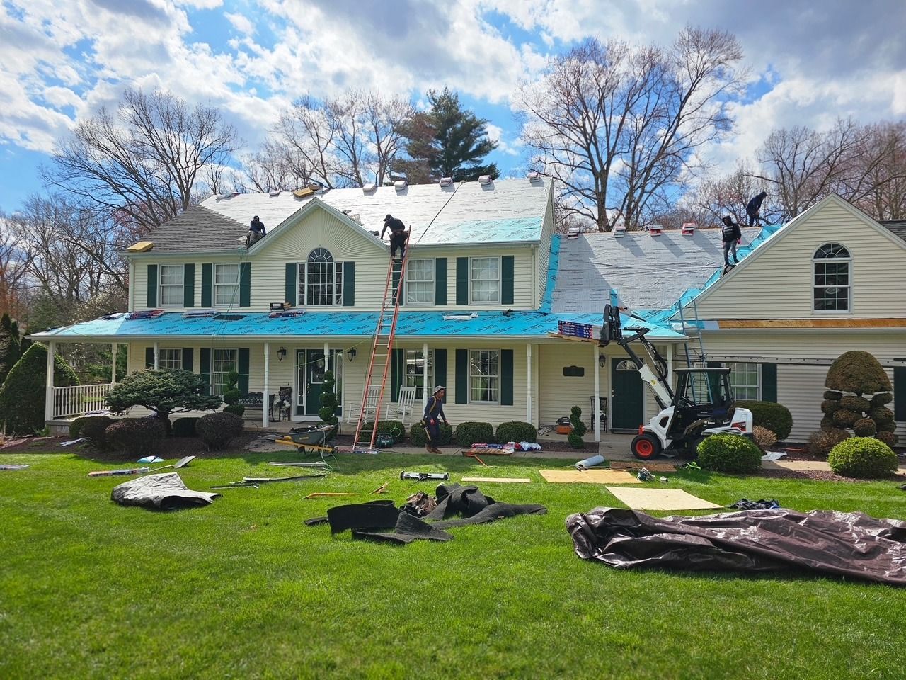 A large white house with a blue roof is being remodeled.