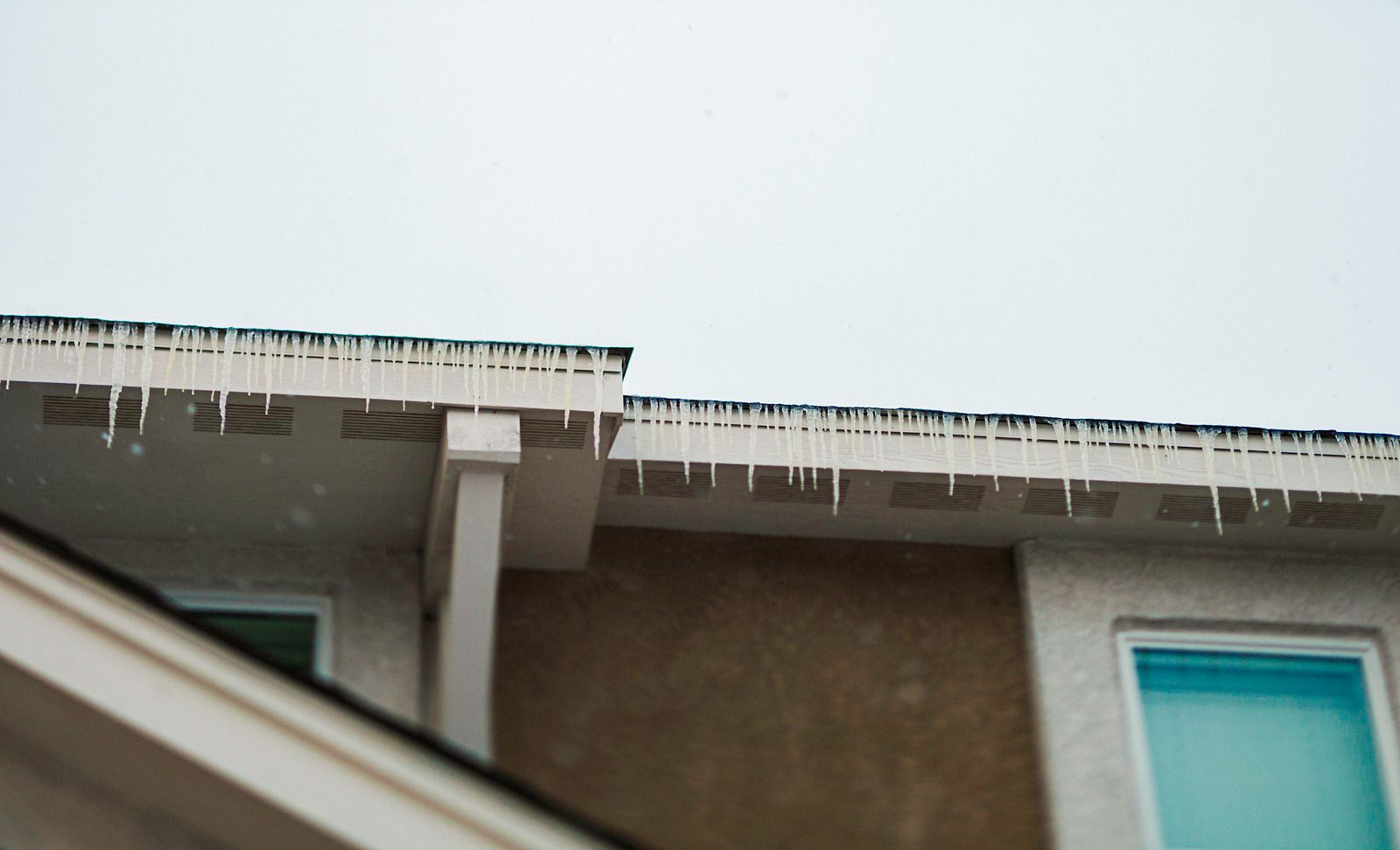 Snow or icicles hanging from a roof edge above a tan building with blue windows