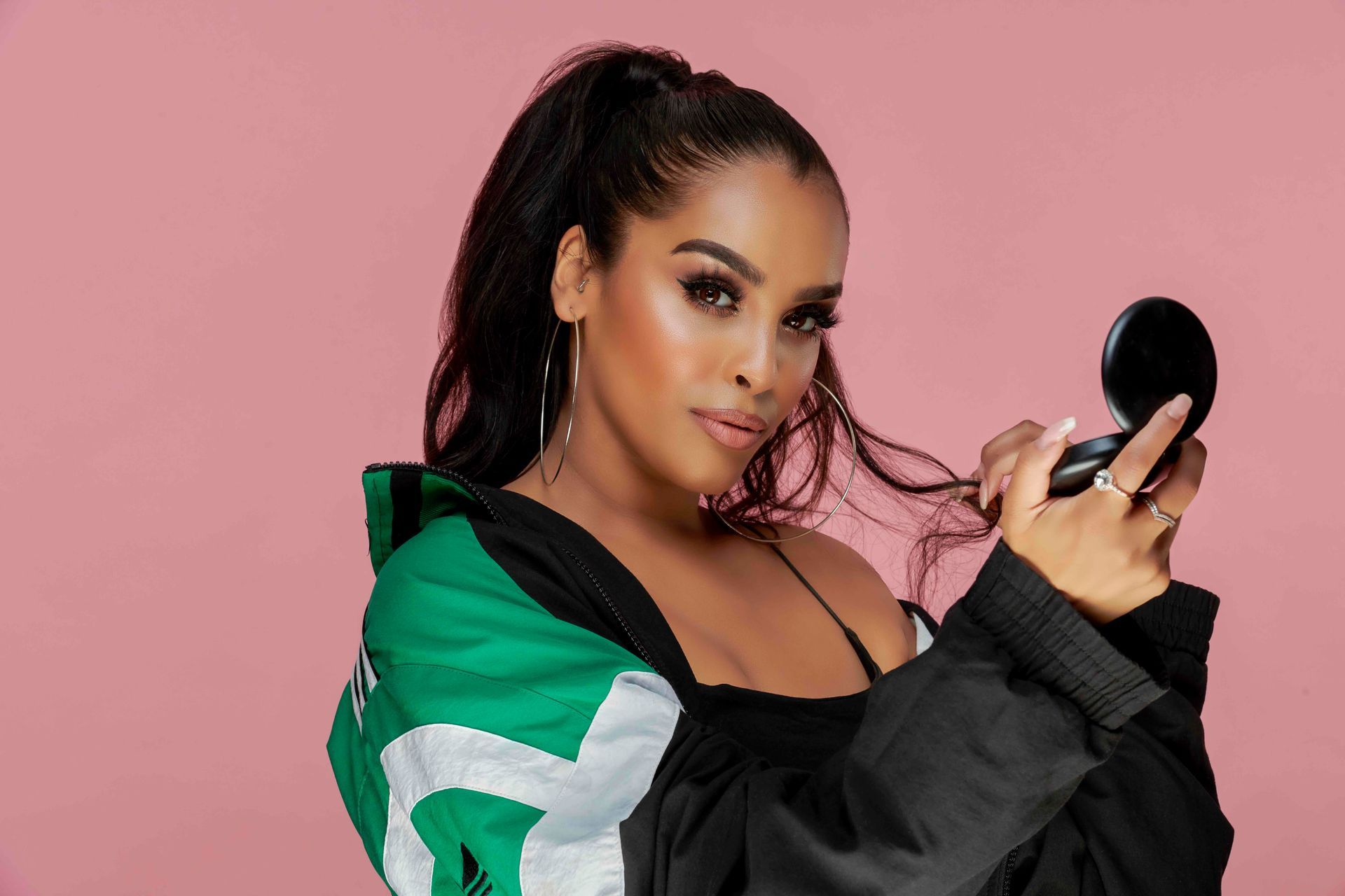 A woman in a green and black jacket is holding a mirror.