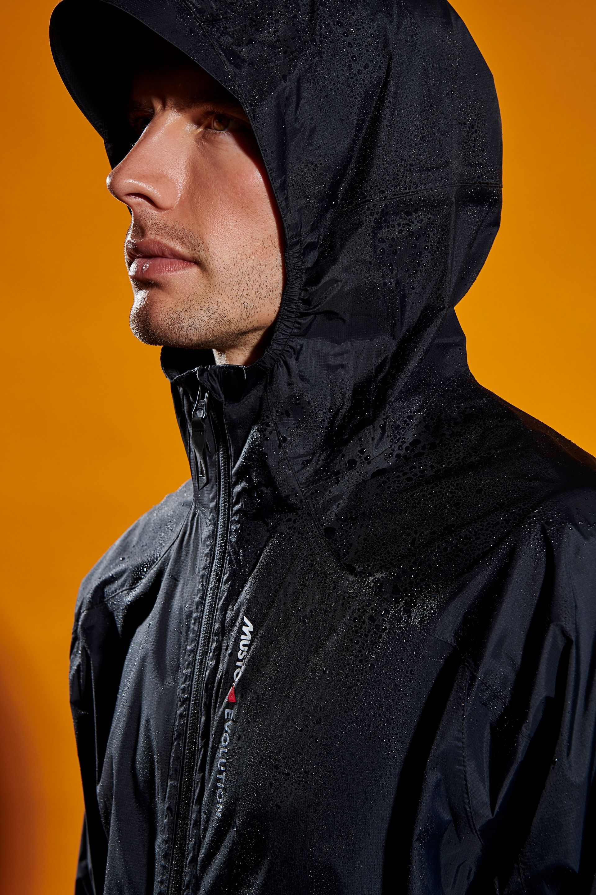 a man wearing a black jacket with a hood is standing in front of an orange background .