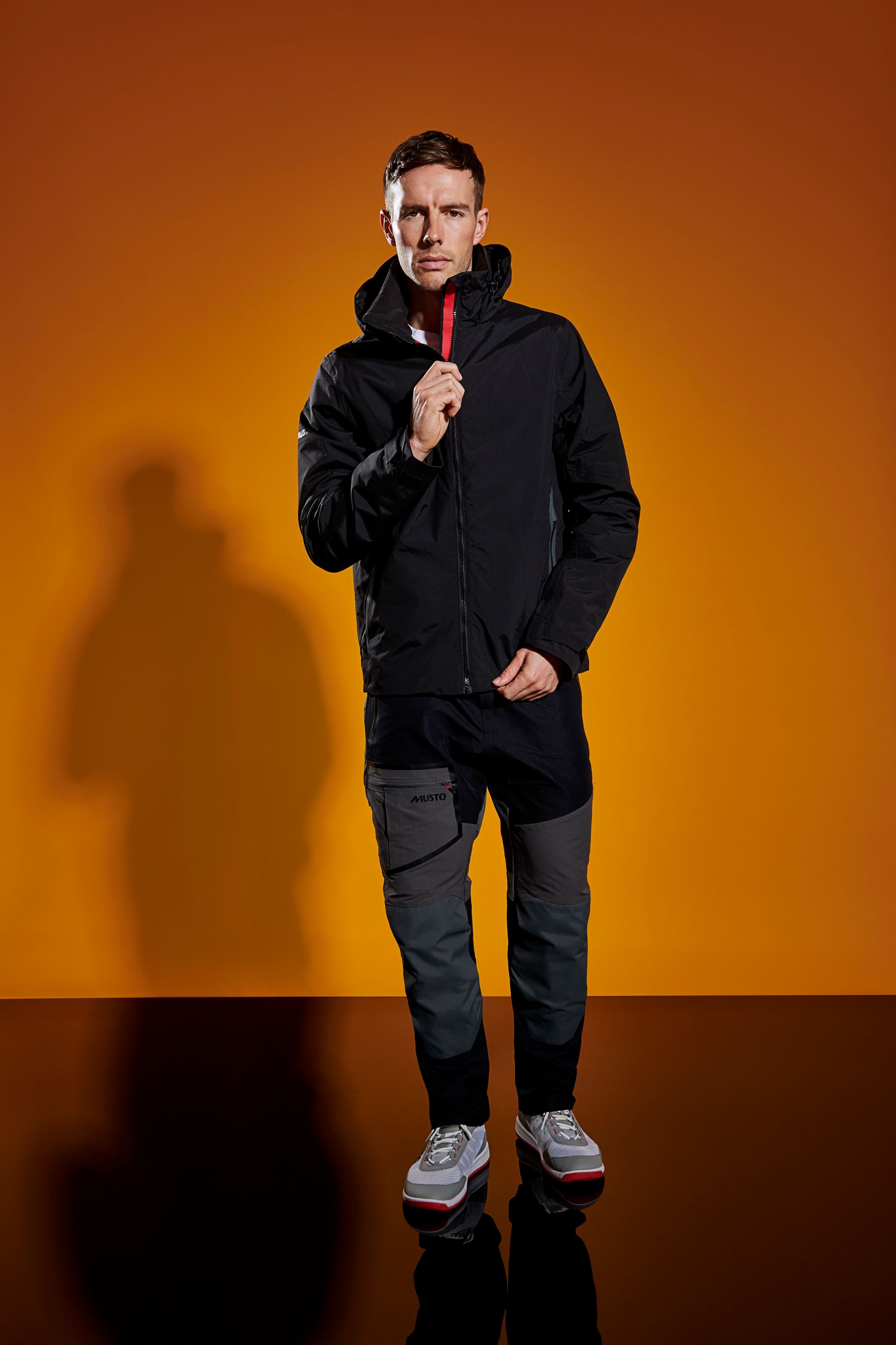 a man wearing a black jacket and gray pants is standing in front of an orange background .