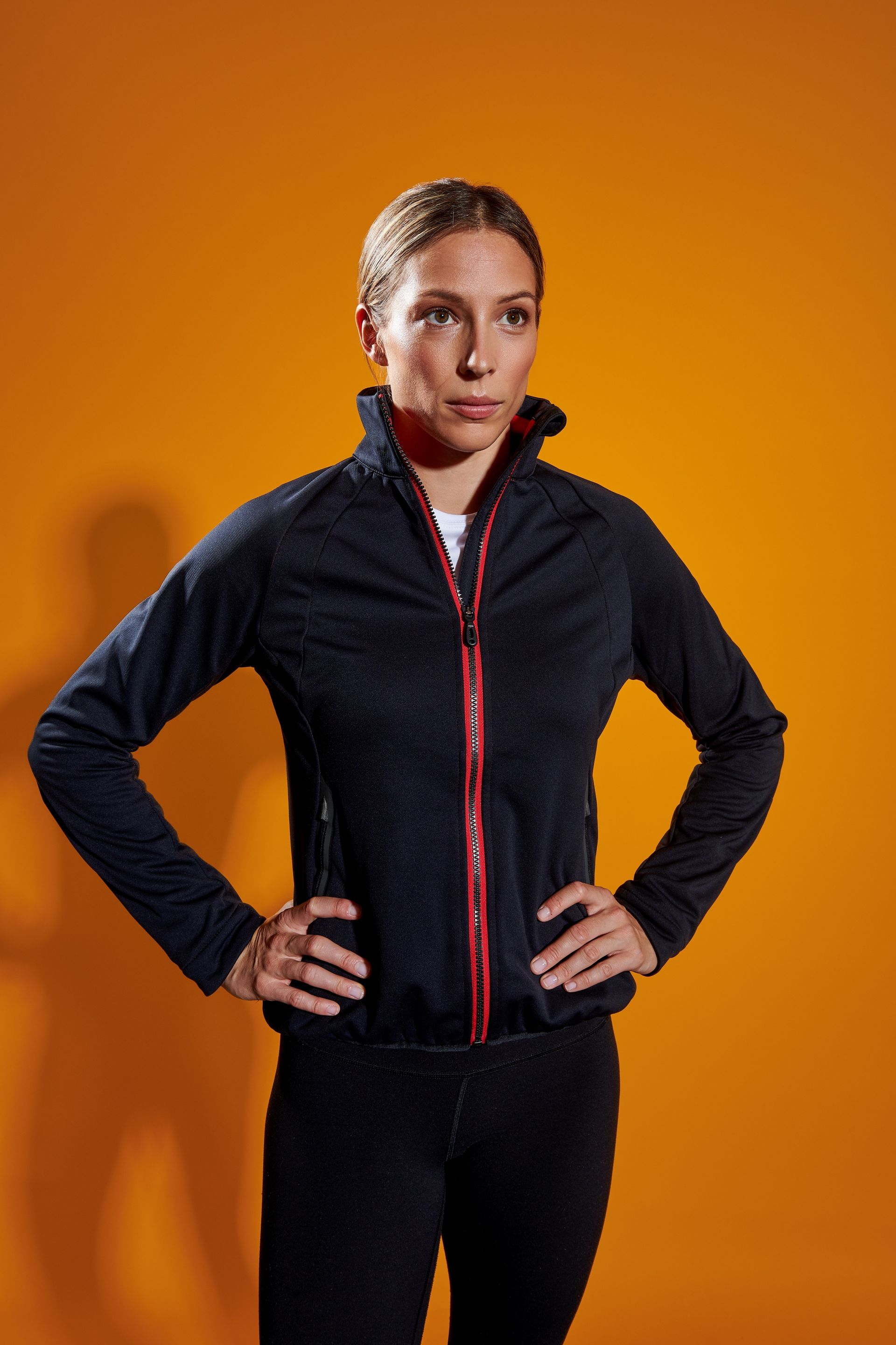 a woman in a black jacket is standing with her hands on her hips .
