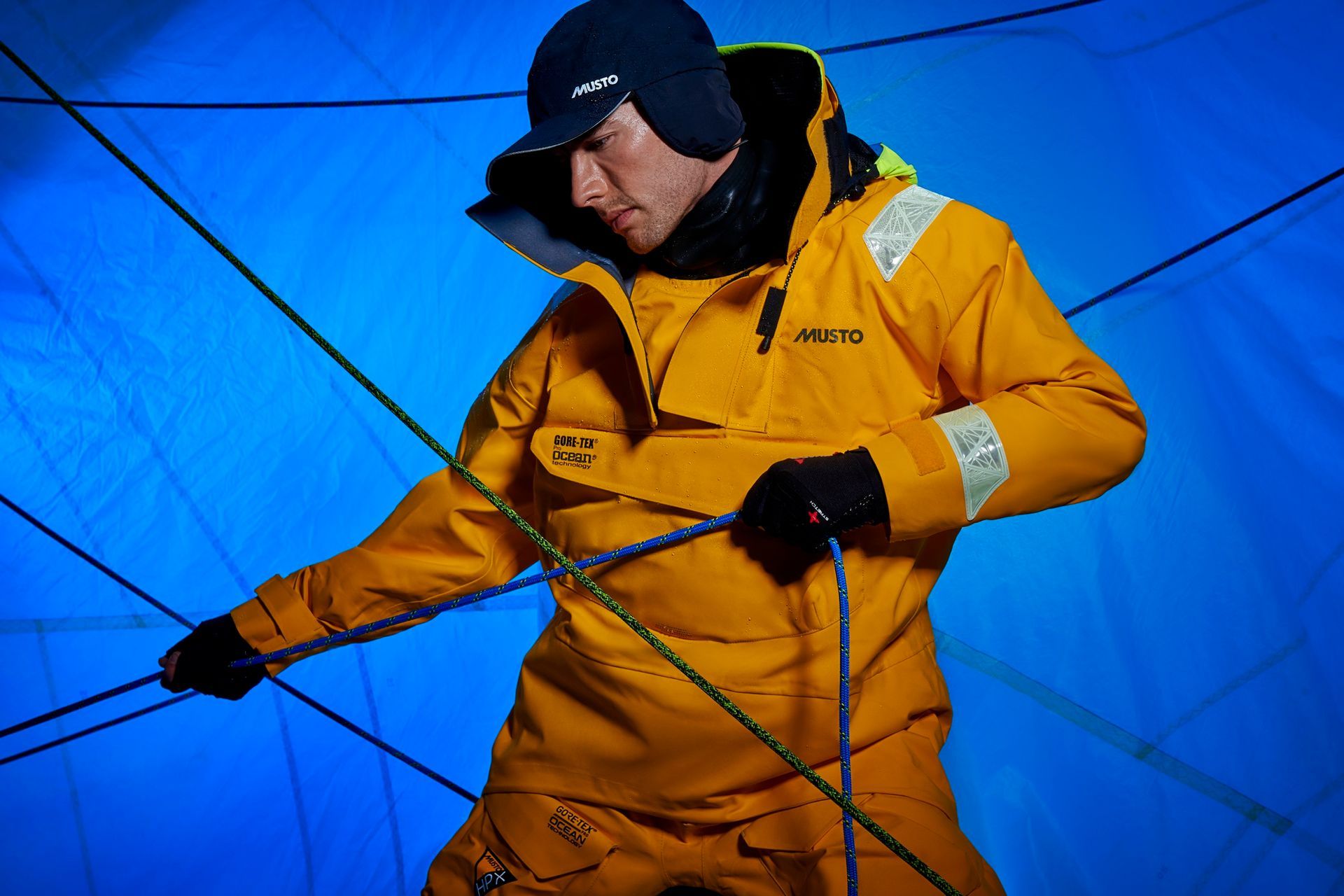 a man in a yellow jacket and hat is holding a rope .