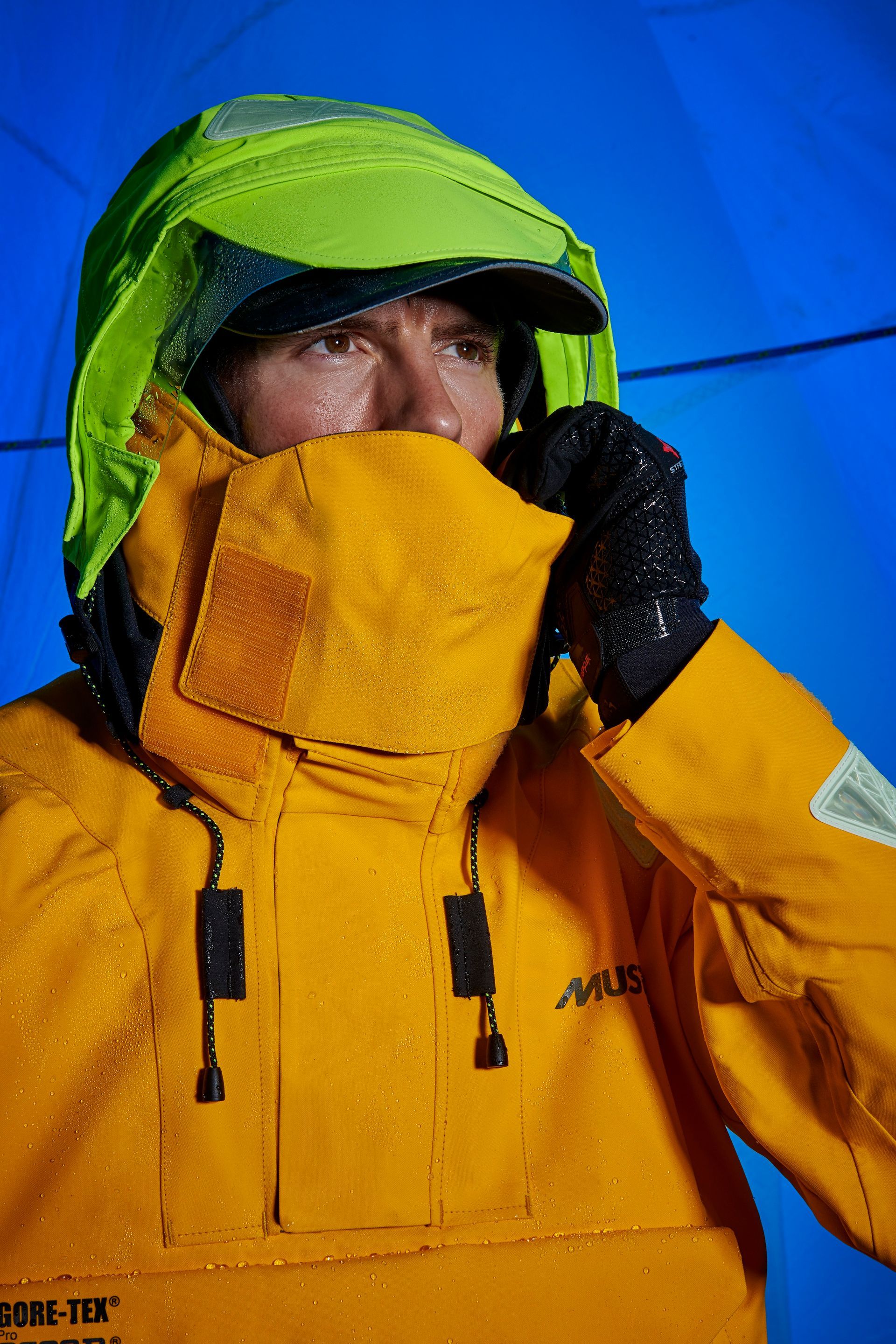a man wearing a yellow jacket and a green hat is covering his mouth with his hand .