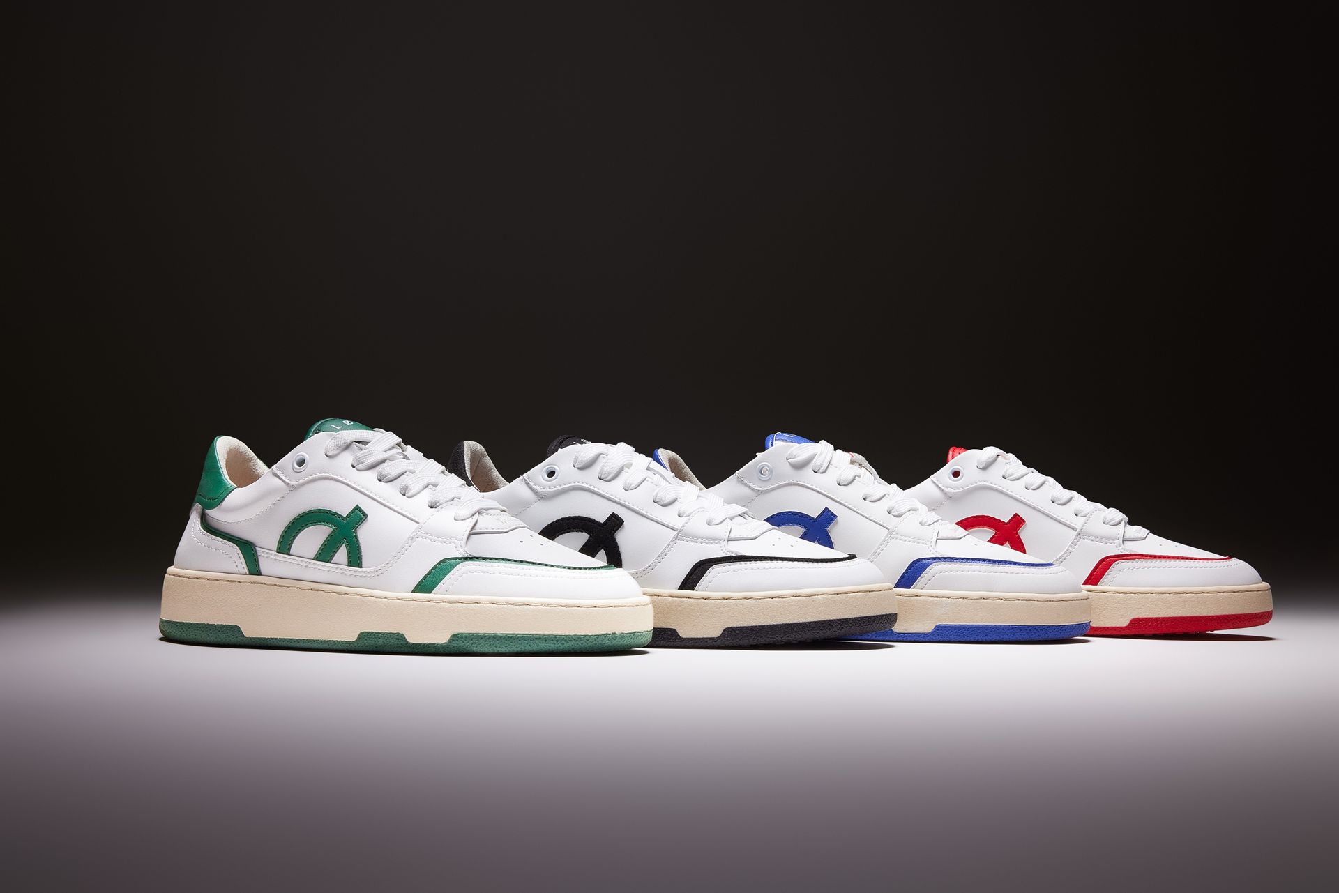four different colored sneakers are lined up on a white surface .