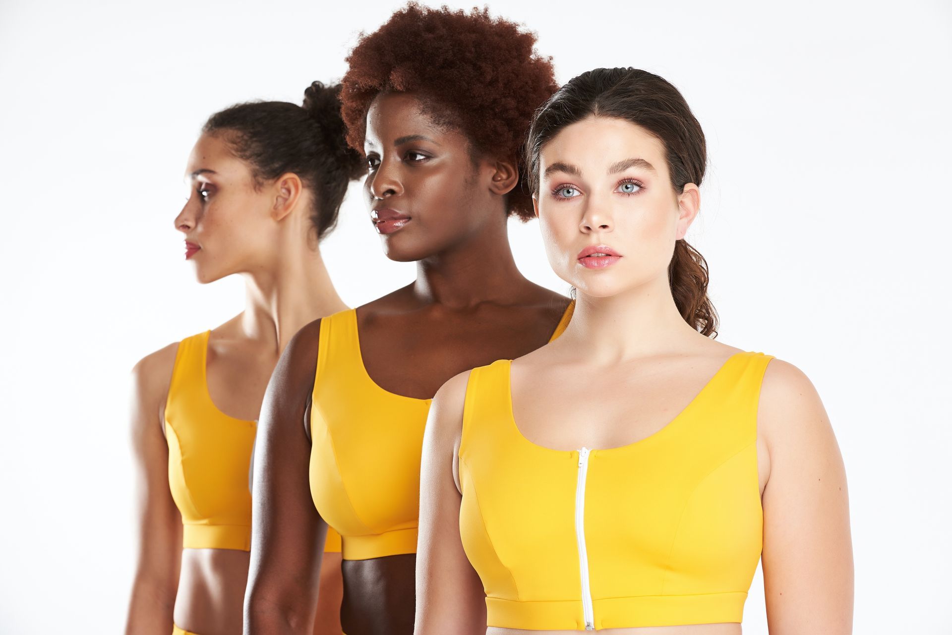 three women are standing next to each other wearing yellow sports bras .