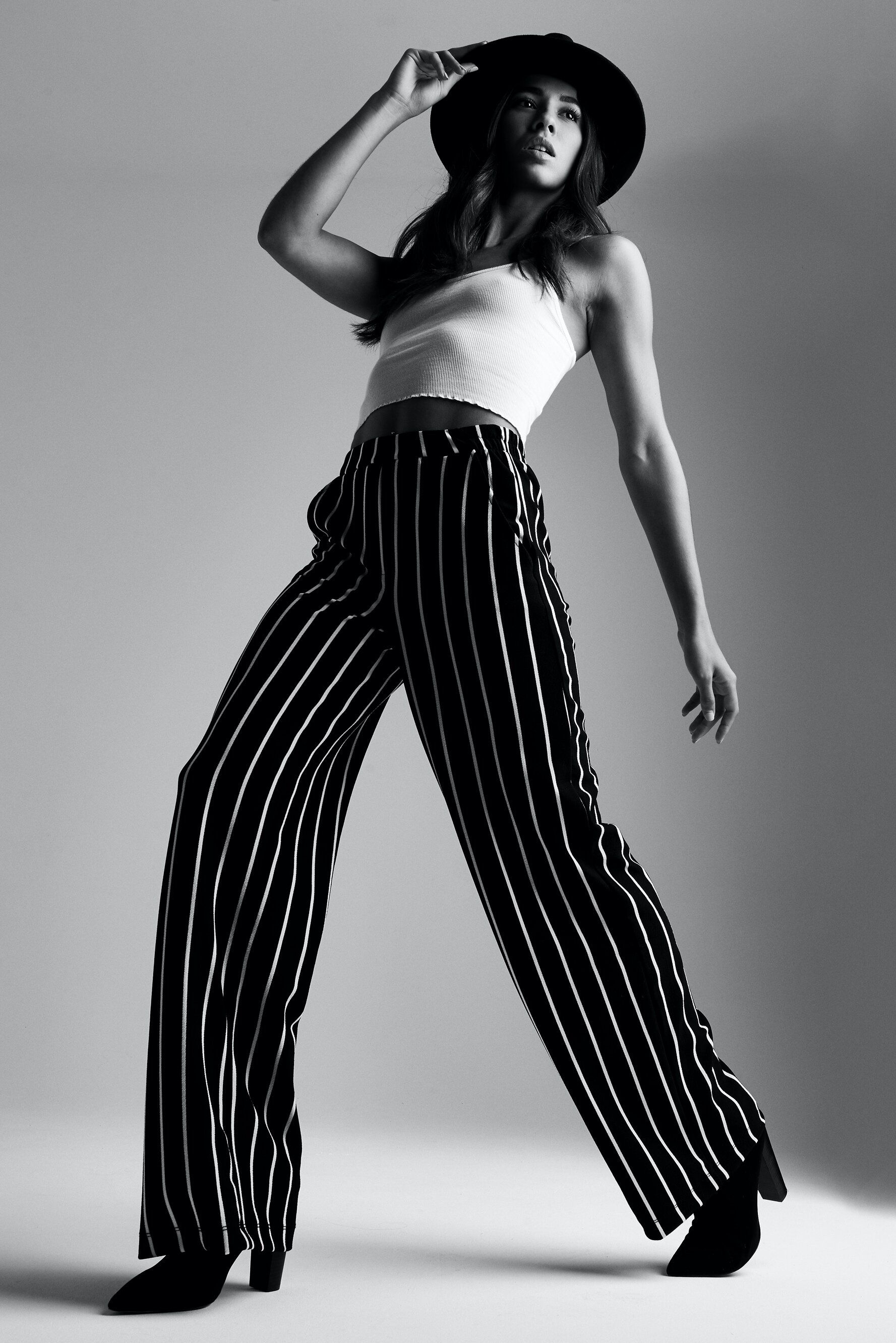 A black and white photo of a woman wearing striped pants and a hat