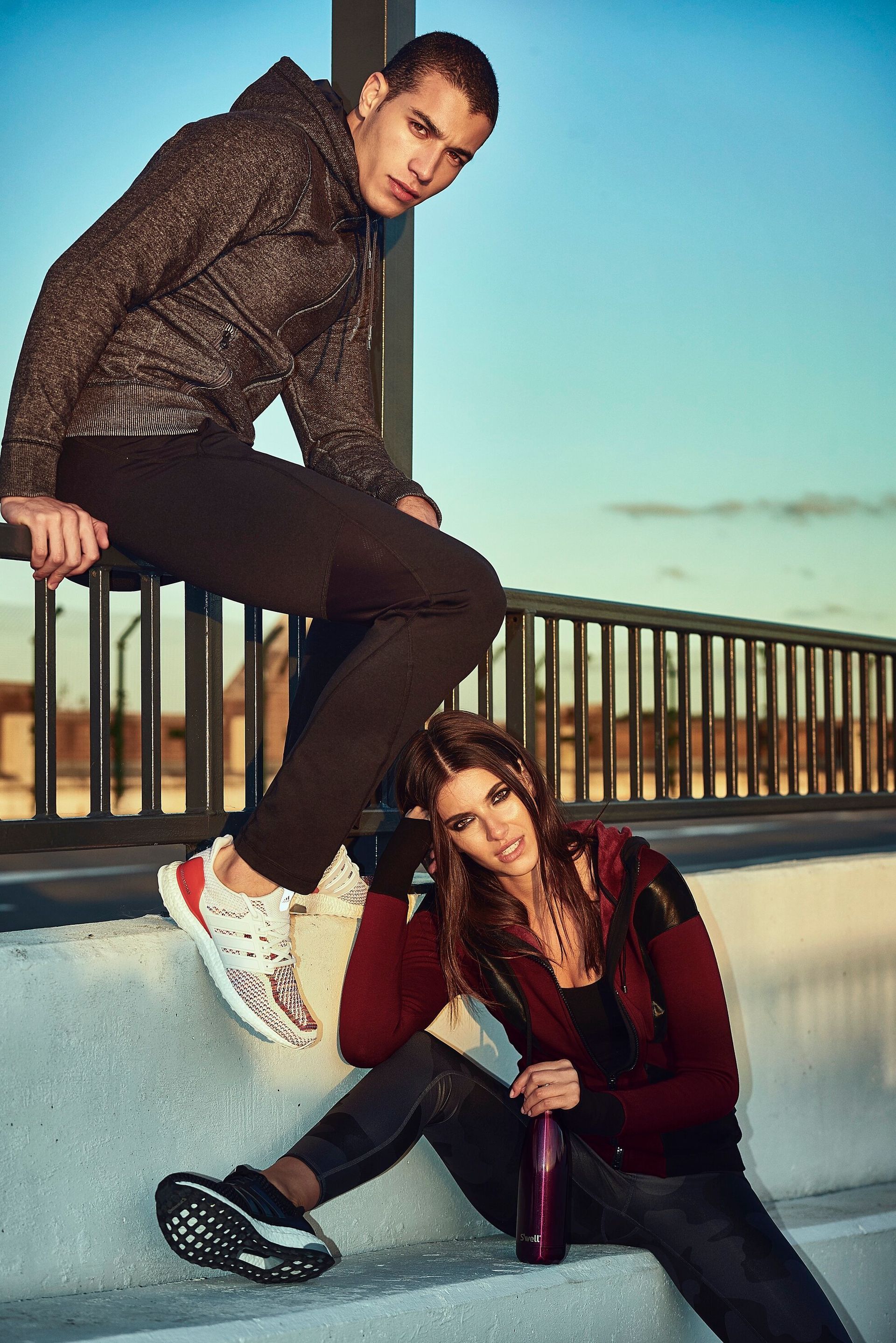 A man is sitting on a railing next to a woman sitting on steps.