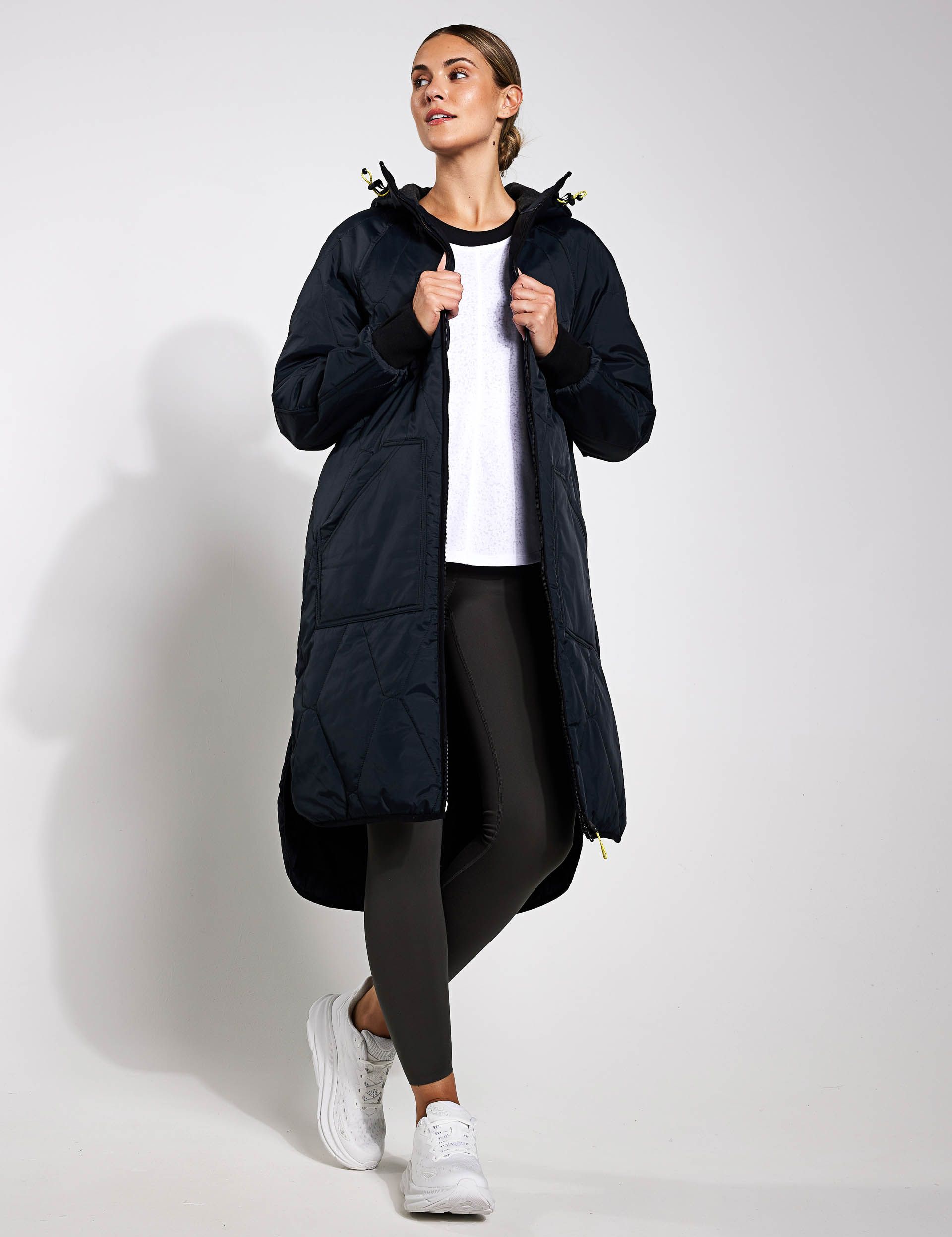 a woman is wearing a long black coat and black leggings .