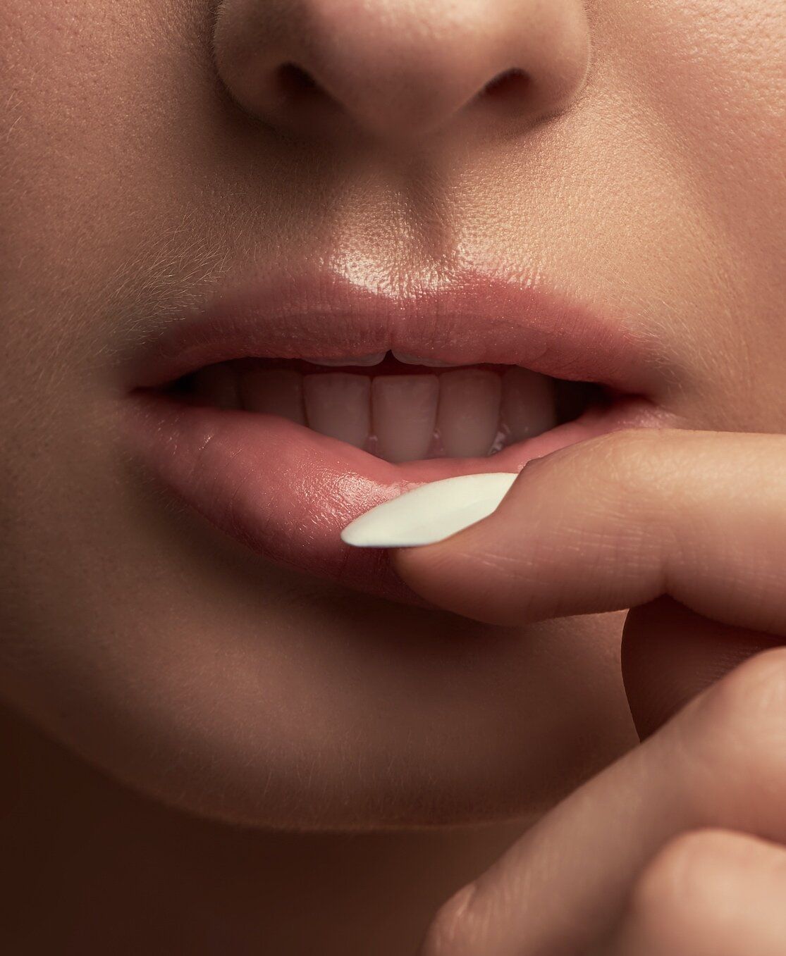 A close up of a woman 's lips with a white nail polish.