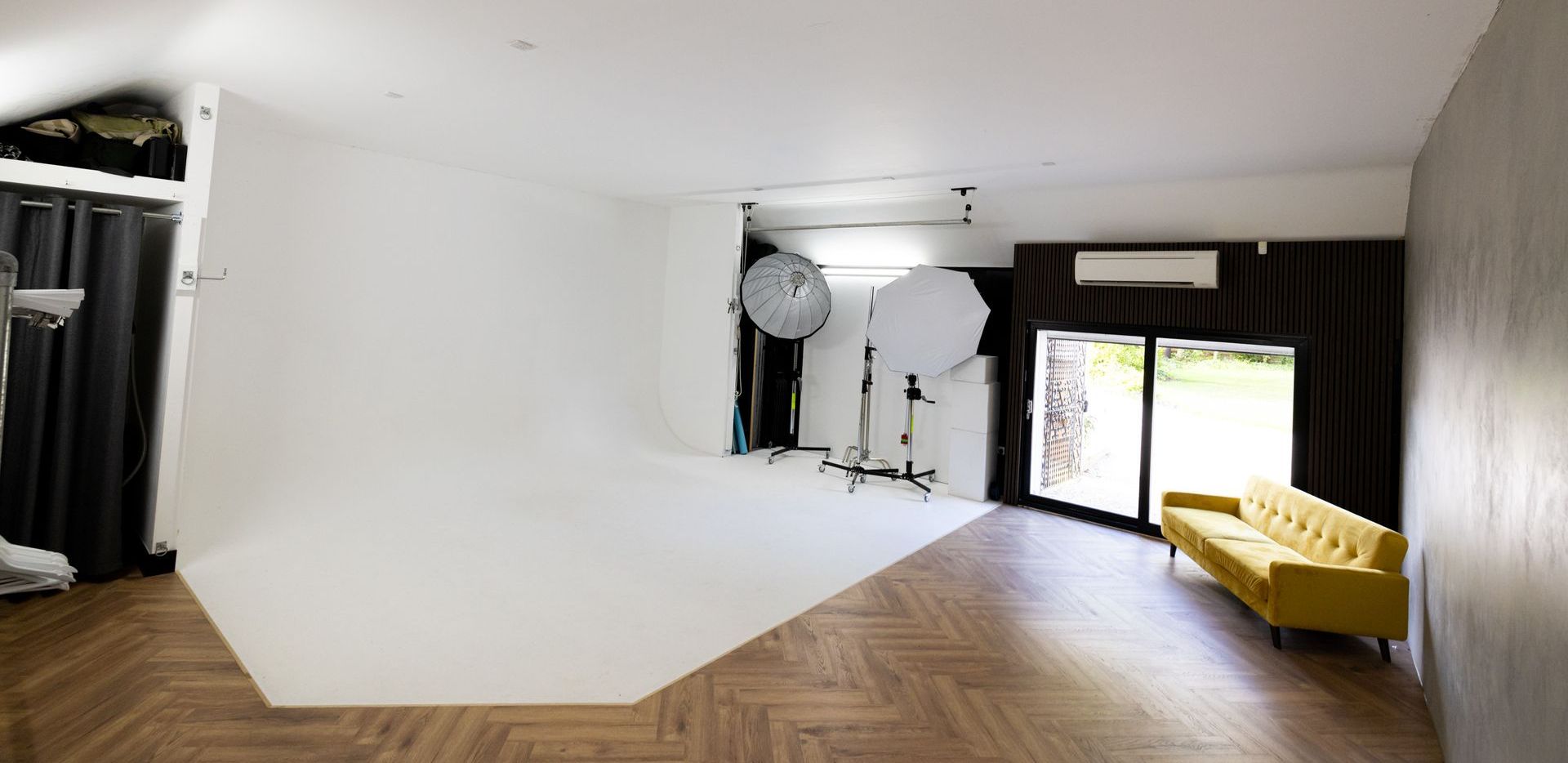 Two men are standing in a living room holding umbrellas and cameras.
