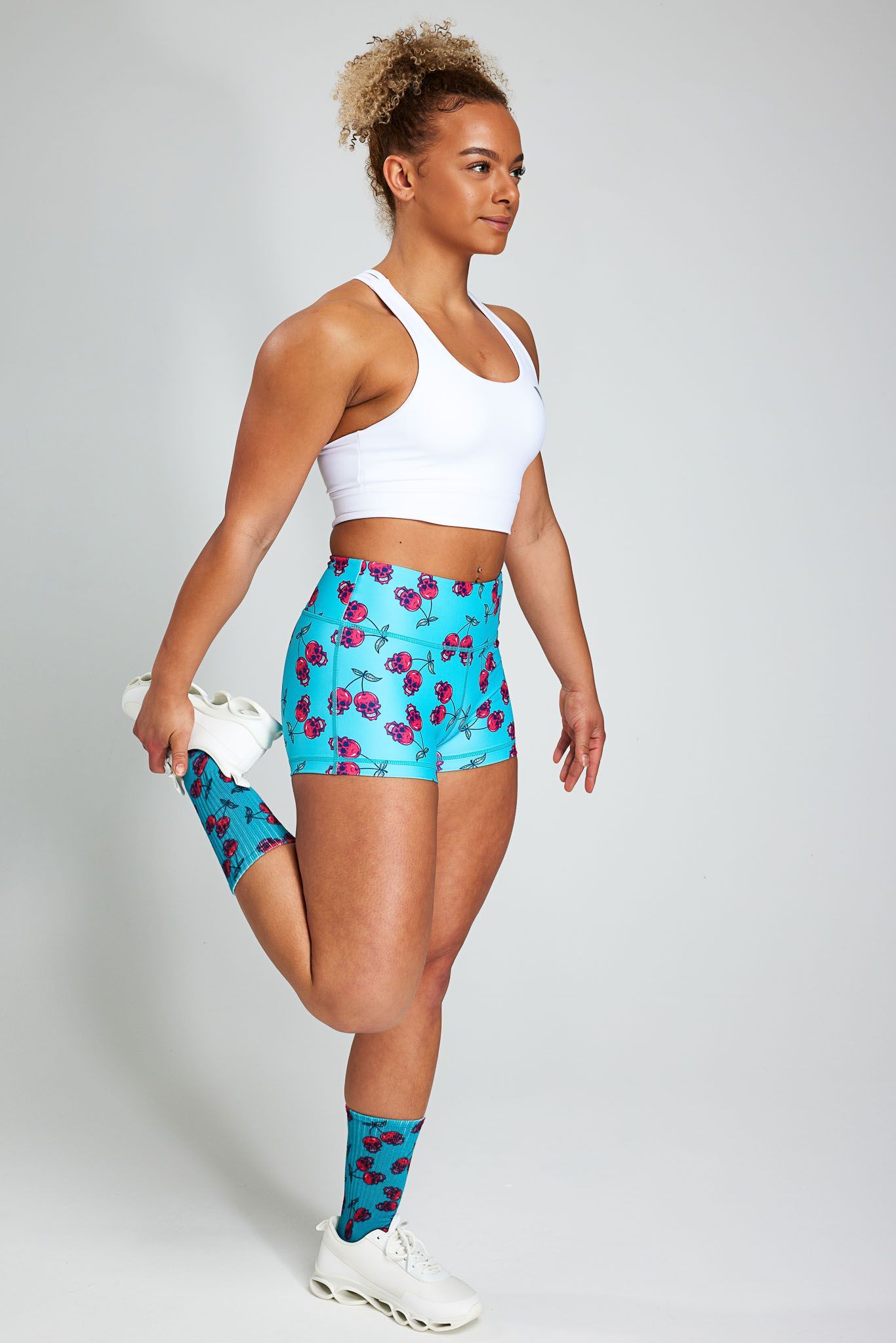 a woman wearing a white tank top and blue shorts is stretching her leg .