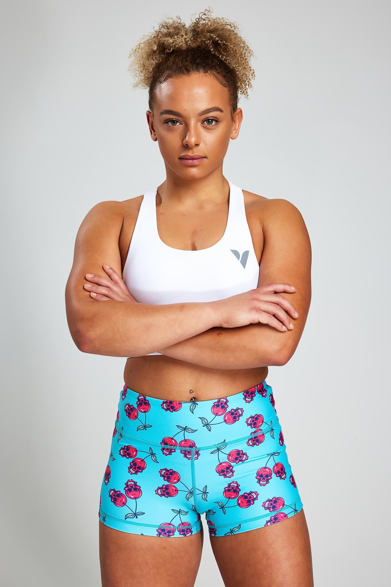 a woman wearing a white sports bra and blue shorts with flowers on them is standing with her arms crossed .