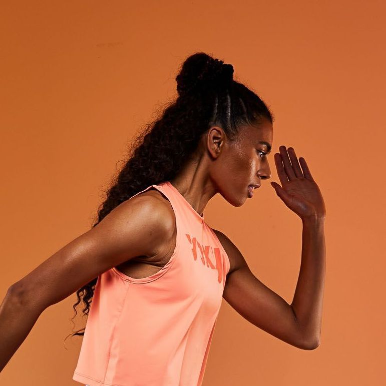 a woman in a pink tank top is running and covering her face with her hand .