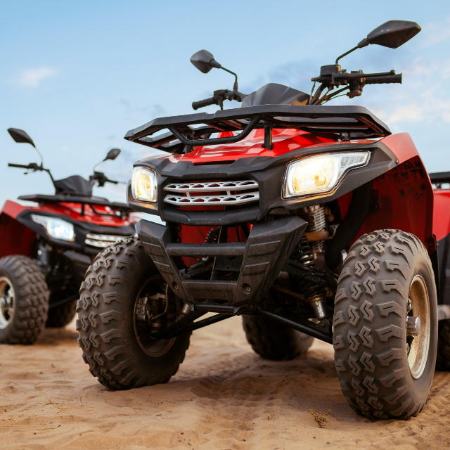 Two red ATVs parked on sandy terrain with a blue sky in the background.