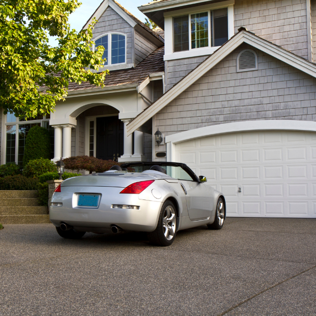 Silver convertible parked in front of a gray house with a two-car garage.