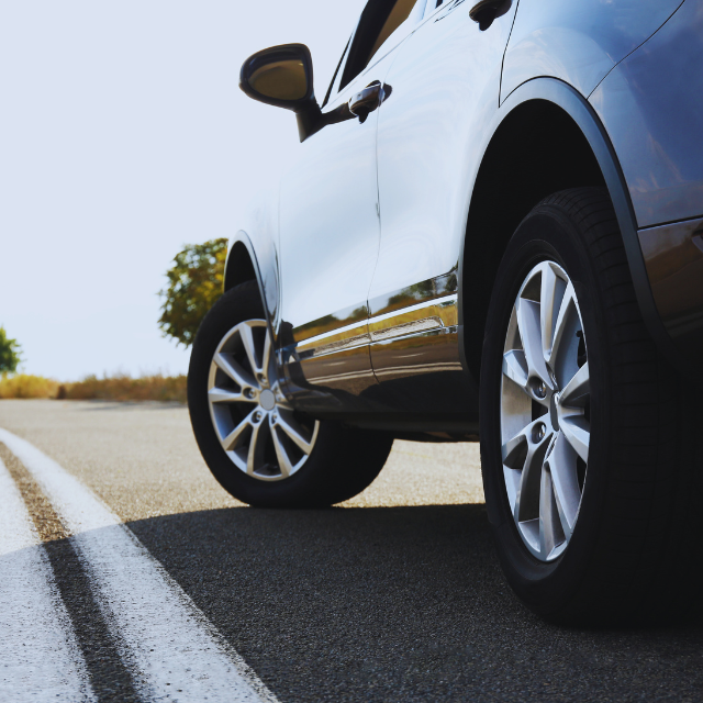 Black SUV parked on a paved road, close-up of the front, white lines visible.
