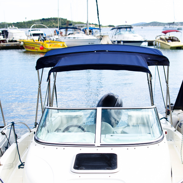 White motorboat with blue canopy docked at a marina with other boats.