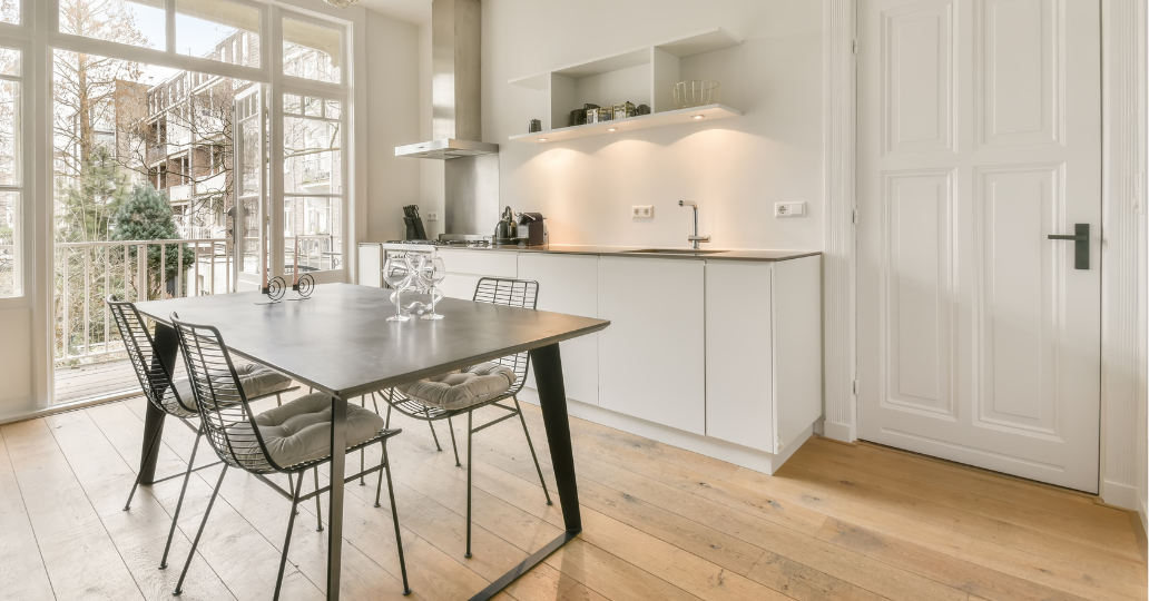 Modern white kitchen with table, chairs, and large window.
