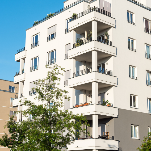 White apartment building with stacked balconies and dark railings, blue sky.