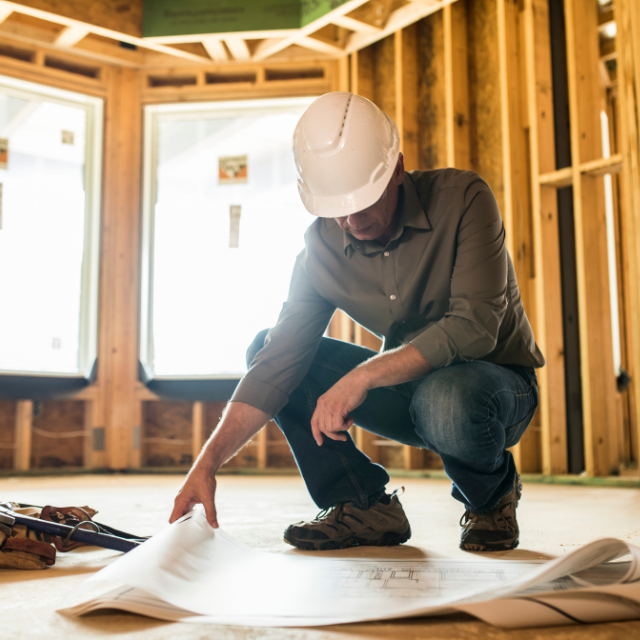 Construction worker in a hard hat reviewing blueprints on a construction site.