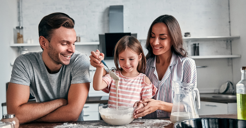 Family in kitchen baking together; smiling, mixing batter.