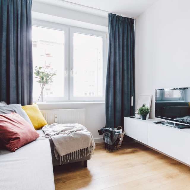 Small living room with couch, window, TV, and blue curtains.