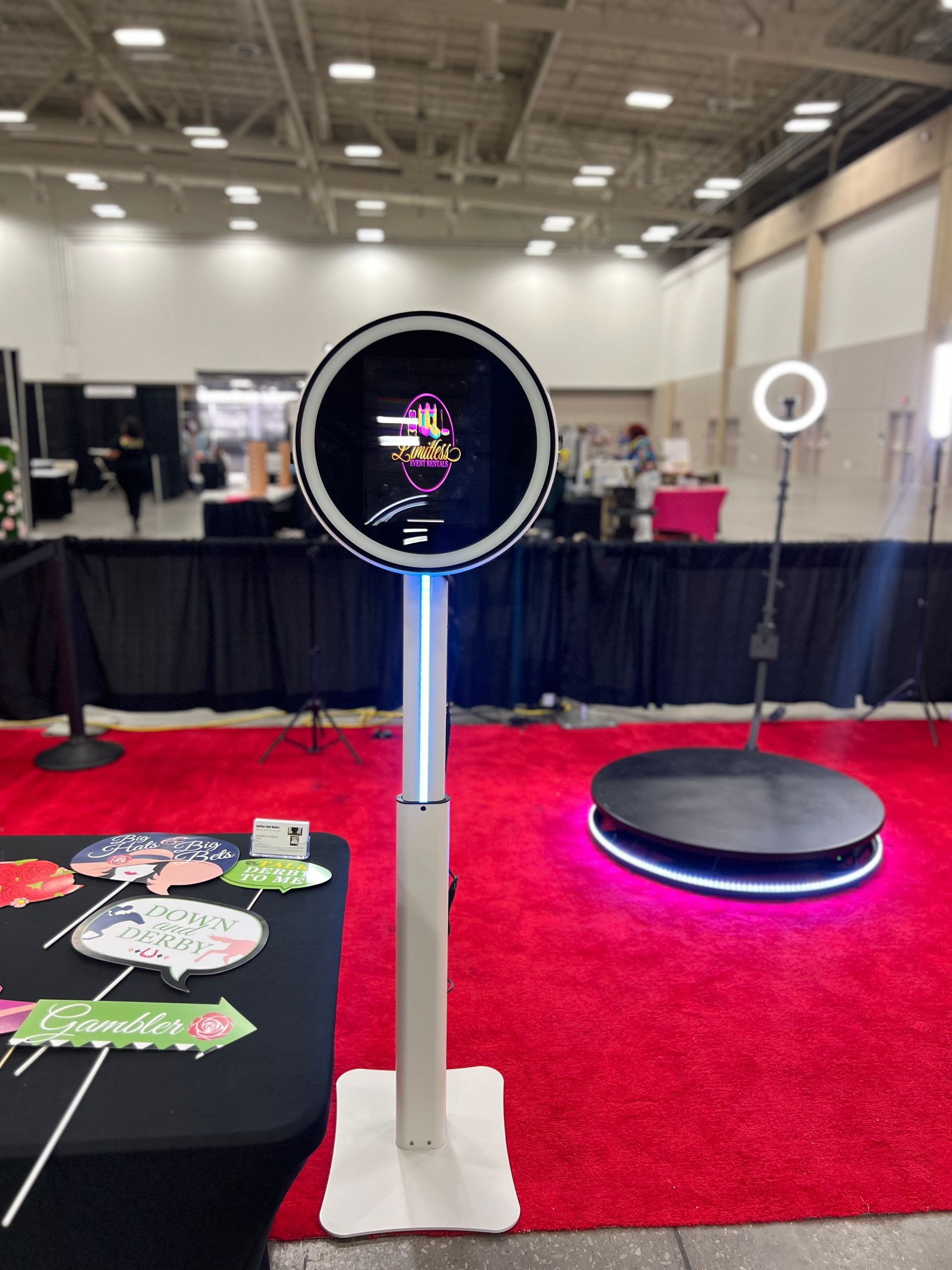 Photo booth setup at an event: circular photo booth, 360 platform, ring light, props on table. Red carpet.