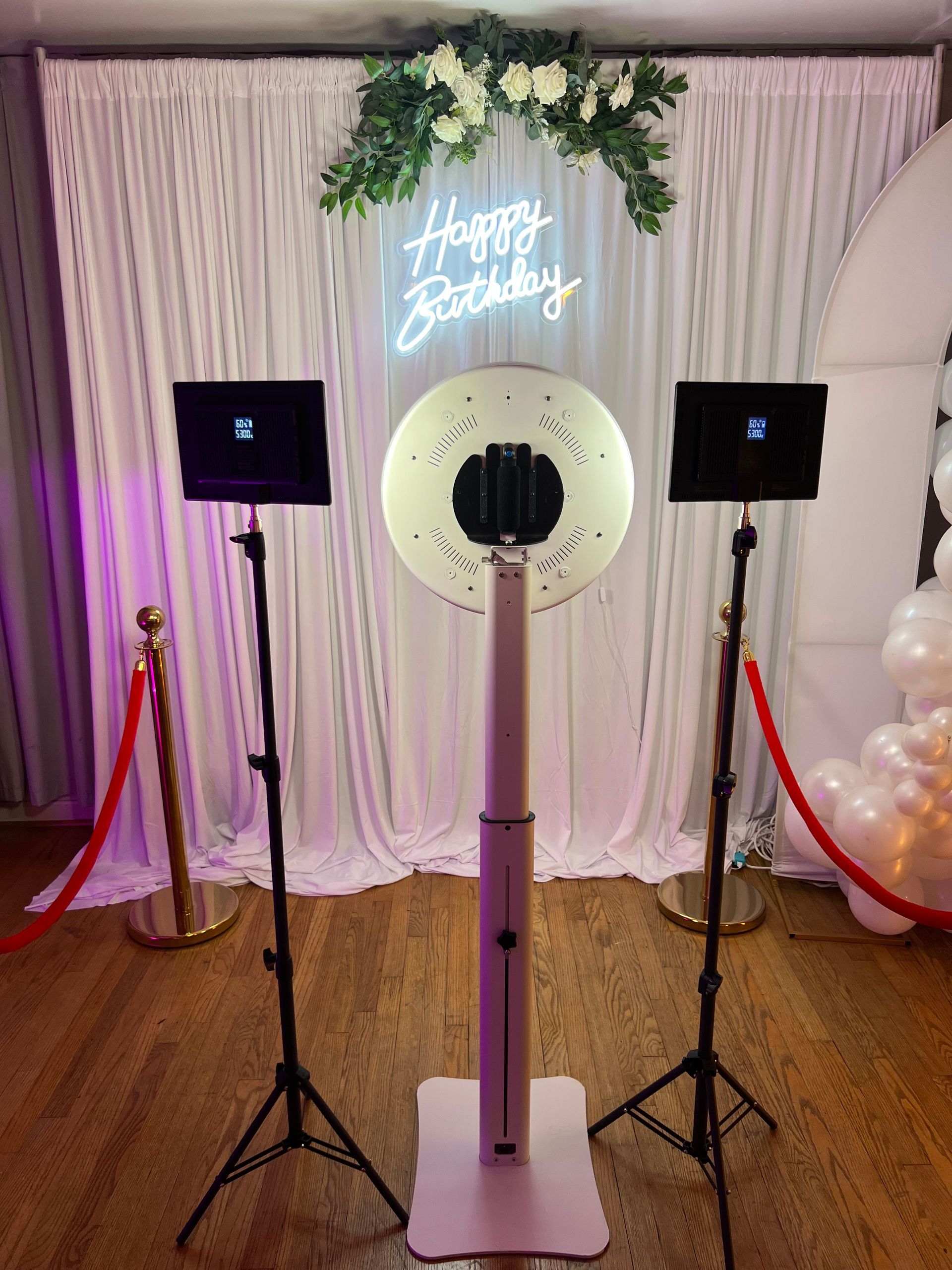 A photo booth with a ring light and balloons in a room.