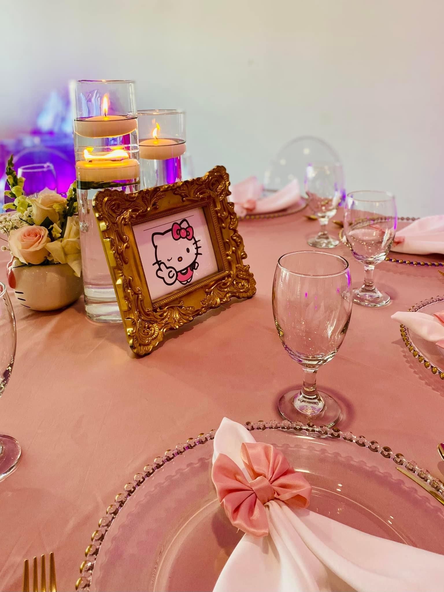 A table with plates , glasses , candles , and a picture frame with a hello kitty picture on it.