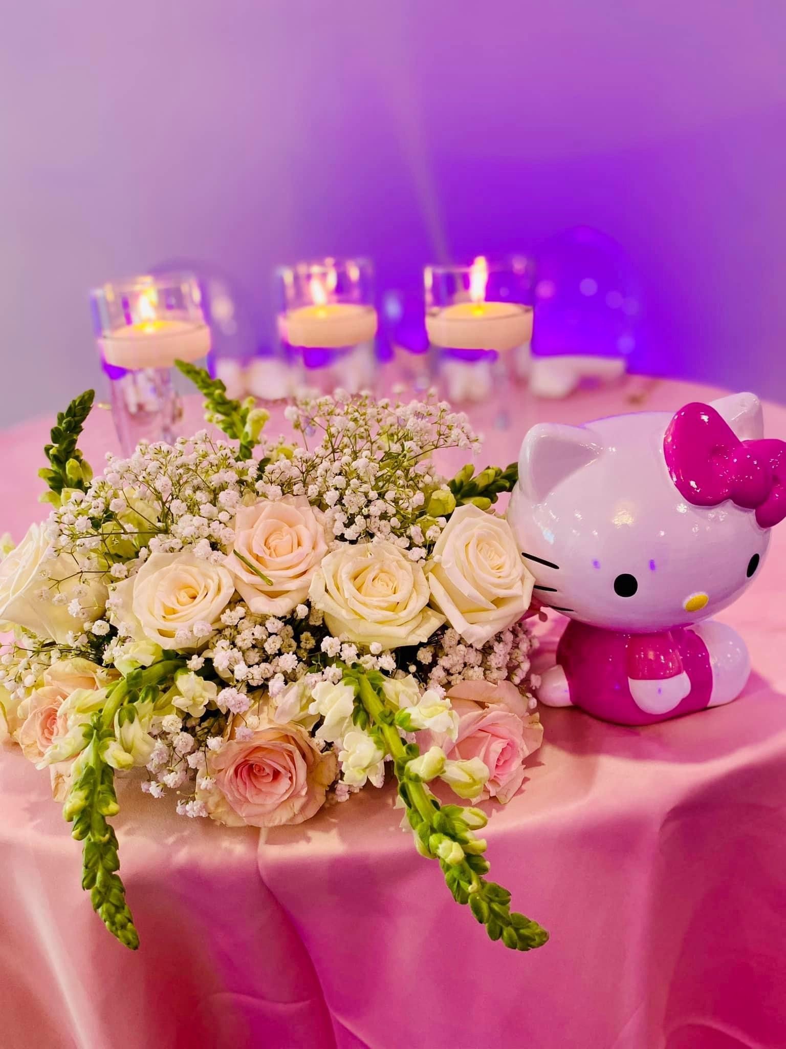 A hello kitty doll is sitting on a table with flowers and candles.