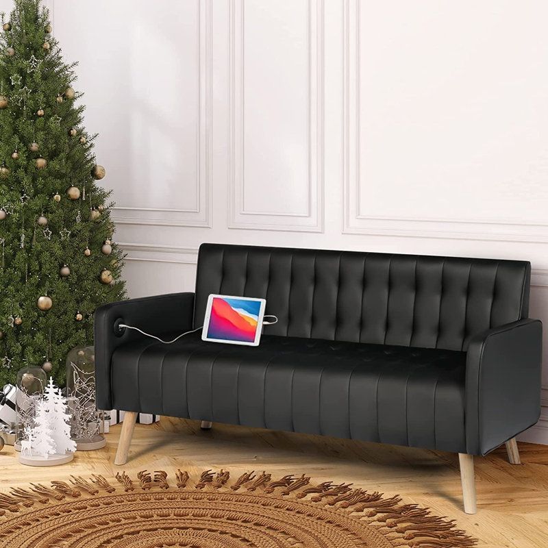 A black couch with a tablet on it next to a christmas tree.