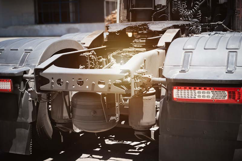 Rear view of a large truck chassis with exposed frame and red taillights in a garage under repair